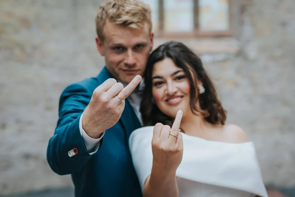 Bride and groom showing middle fingers with rings