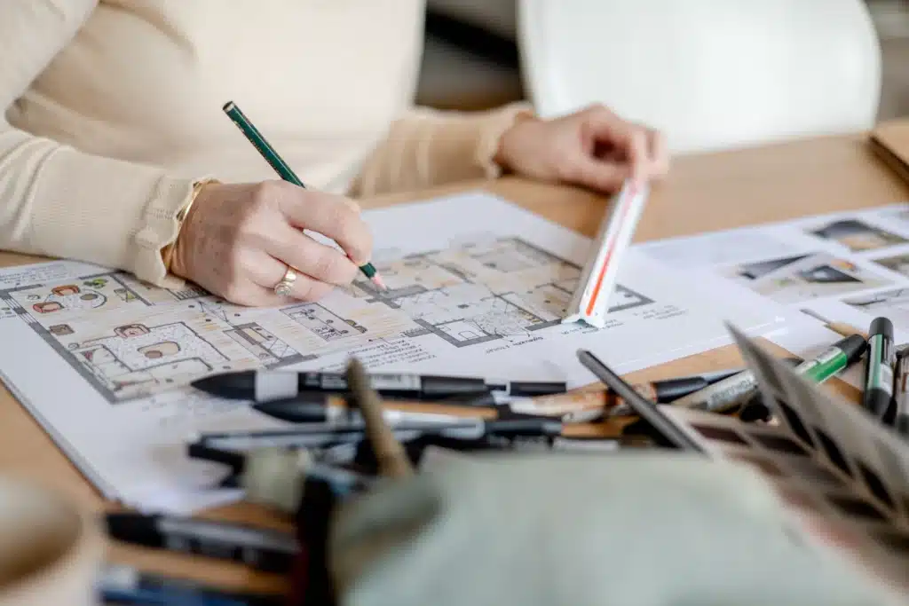 Person sketching architectural floor plan at desk
