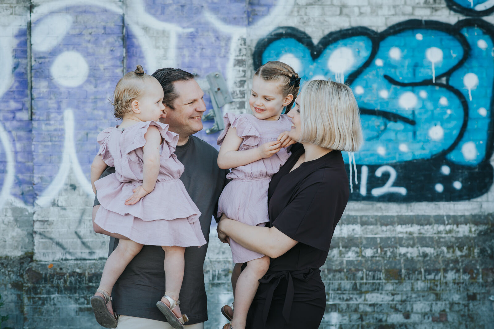 Familie portretfoto van ouders met twee kleine meisjes in roze jurken tegen graffiti muur, professionele portretfotografie door Vera Wapstra fotograaf Friesland